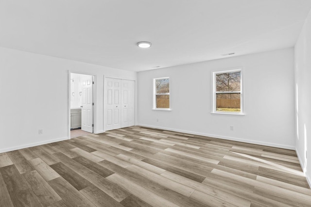 unfurnished bedroom with ensuite bathroom and light wood-type flooring