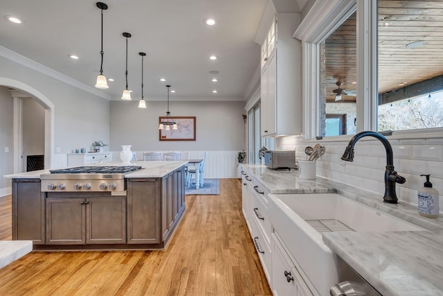 kitchen featuring pendant lighting, sink, white cabinetry, light stone counters, and stainless steel gas stovetop