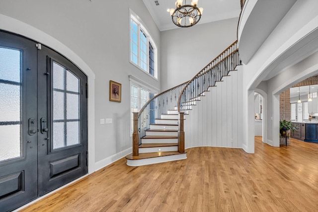 foyer entrance with crown molding, light hardwood / wood-style floors, french doors, and a chandelier