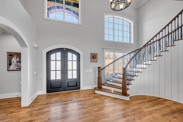 entryway with a towering ceiling, hardwood / wood-style floors, a notable chandelier, and french doors