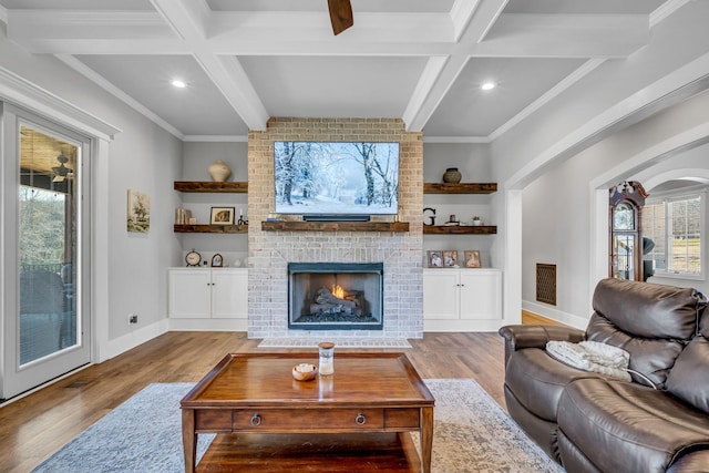 living room featuring a brick fireplace, built in shelves, light hardwood / wood-style flooring, and beamed ceiling