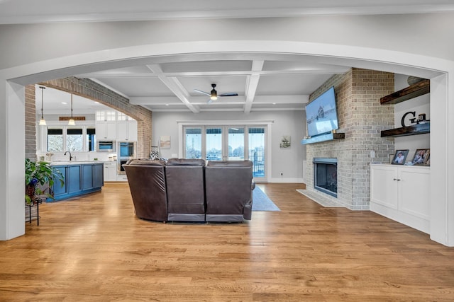 living room featuring coffered ceiling, sink, beam ceiling, light hardwood / wood-style flooring, and a fireplace