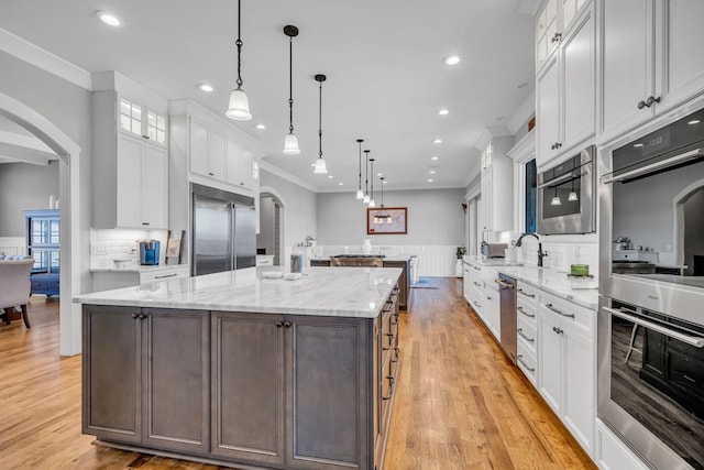 kitchen with a large island, pendant lighting, white cabinetry, backsplash, and stainless steel appliances