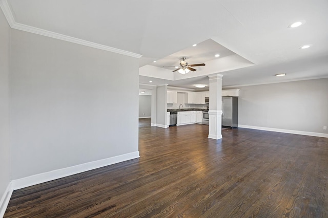 unfurnished living room with ceiling fan, ornamental molding, a tray ceiling, and ornate columns