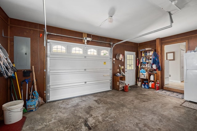 garage with white refrigerator, electric panel, and wood walls