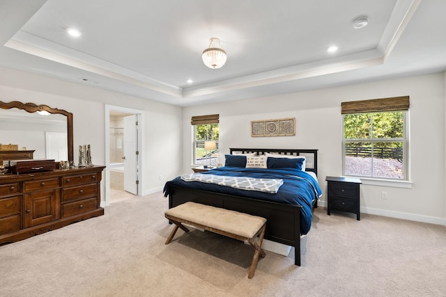 bedroom featuring a raised ceiling, connected bathroom, and light colored carpet