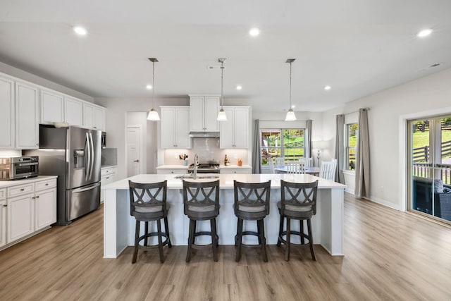 kitchen with a kitchen island with sink, decorative light fixtures, white cabinets, and a kitchen bar