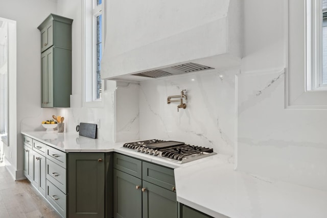 kitchen featuring stainless steel gas cooktop, tasteful backsplash, light stone counters, custom range hood, and light hardwood / wood-style floors