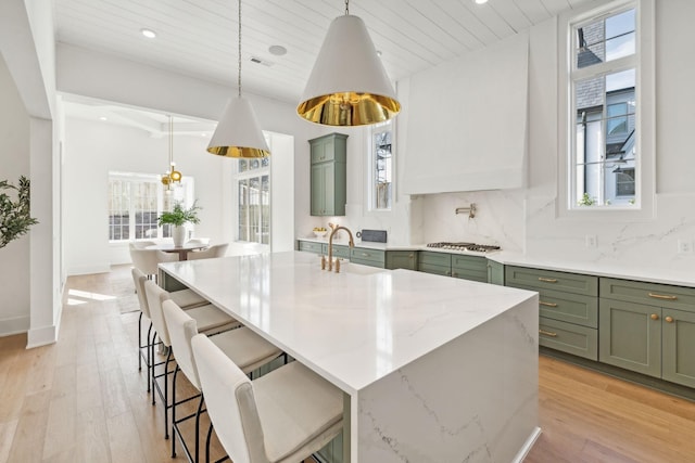 kitchen featuring sink, a kitchen island with sink, tasteful backsplash, green cabinetry, and decorative light fixtures