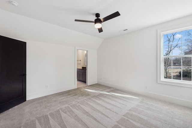 unfurnished bedroom featuring lofted ceiling, connected bathroom, multiple windows, and ceiling fan