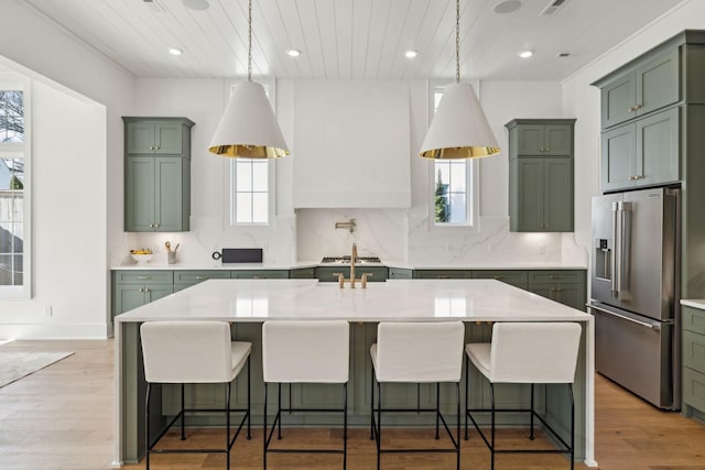 kitchen featuring a kitchen breakfast bar, a kitchen island with sink, high end refrigerator, and light stone counters