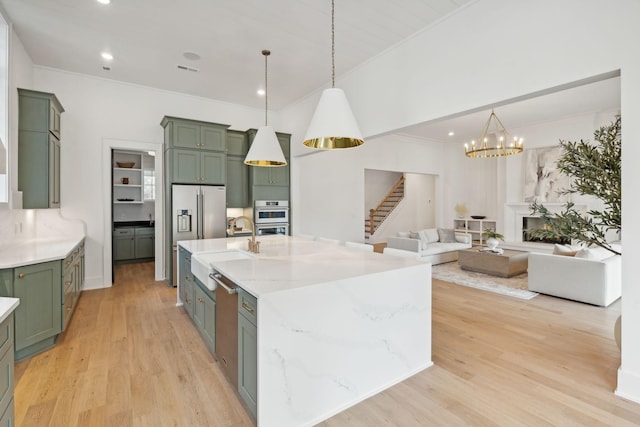 kitchen with pendant lighting, sink, light stone countertops, green cabinetry, and a center island with sink