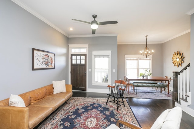 living room featuring dark wood-type flooring, ornamental molding, and ceiling fan with notable chandelier