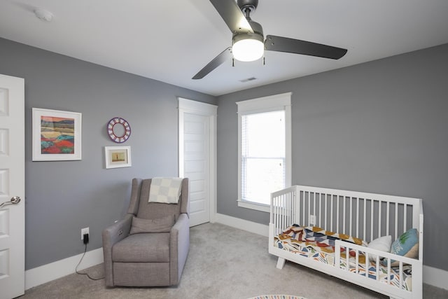 bedroom featuring a nursery area, light colored carpet, and ceiling fan