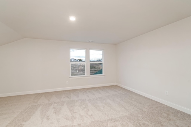 unfurnished room with light colored carpet, vaulted ceiling, visible vents, and baseboards