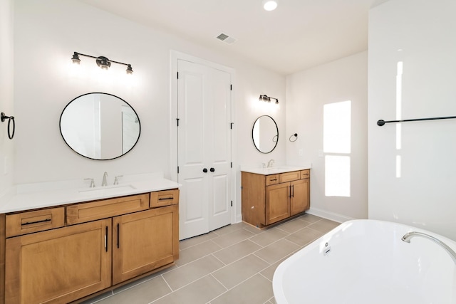 full bathroom featuring a freestanding bath, two vanities, a sink, and visible vents