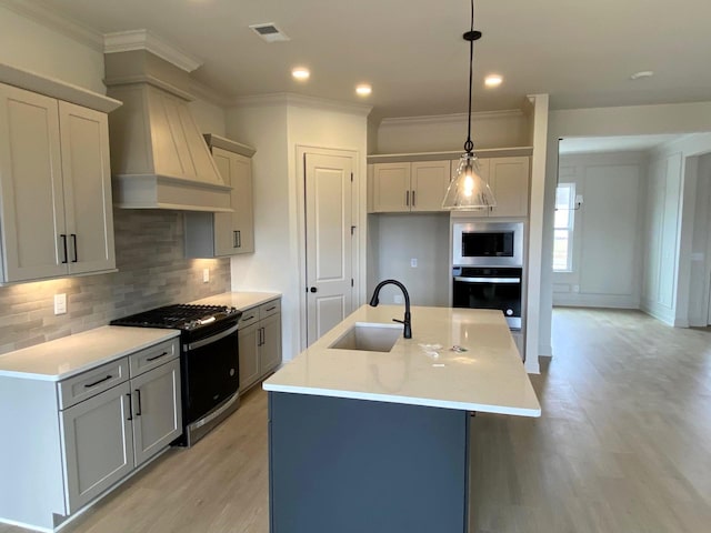 kitchen featuring a center island with sink, stainless steel appliances, light countertops, hanging light fixtures, and a sink