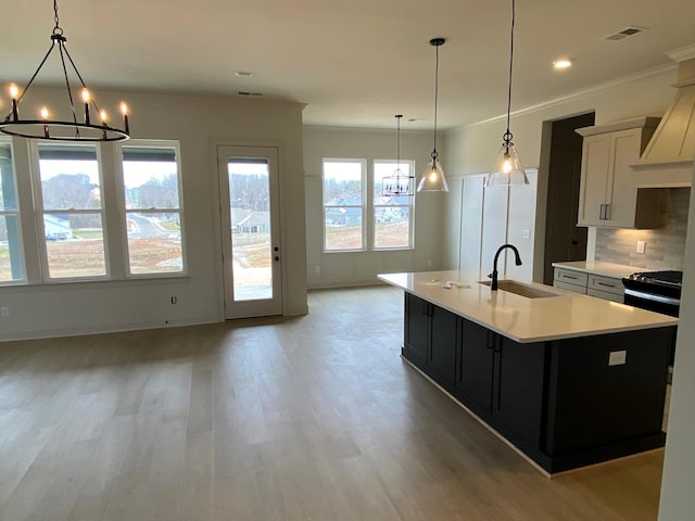 kitchen featuring a sink, white cabinets, light countertops, a center island with sink, and pendant lighting