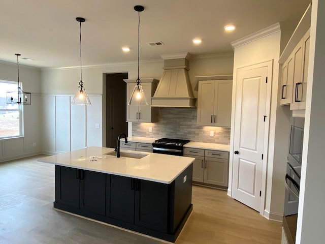 kitchen with light countertops, appliances with stainless steel finishes, a sink, an island with sink, and premium range hood