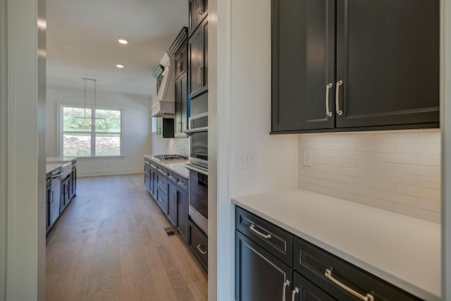 kitchen with tasteful backsplash, appliances with stainless steel finishes, hanging light fixtures, and light wood-type flooring