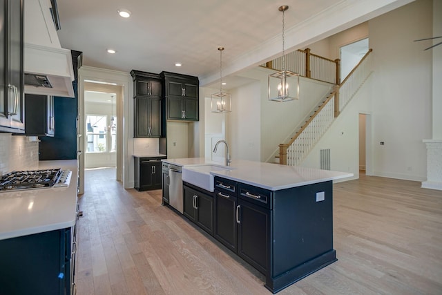 kitchen featuring sink, appliances with stainless steel finishes, a kitchen island with sink, light hardwood / wood-style floors, and decorative light fixtures