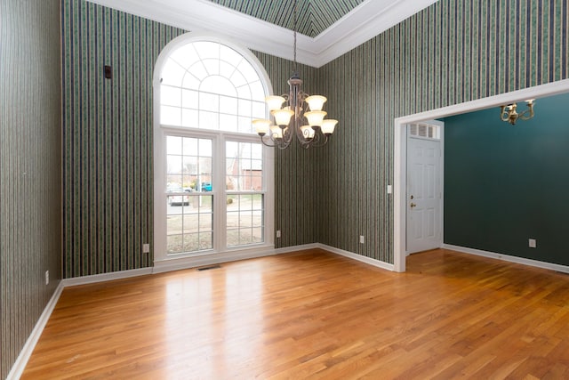 empty room with an inviting chandelier, hardwood / wood-style floors, and ornamental molding