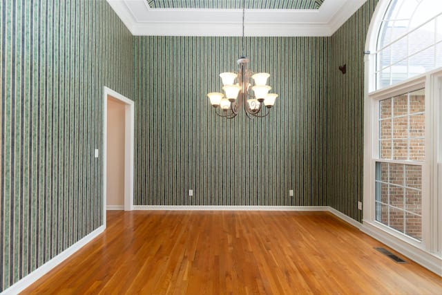 empty room with ornamental molding, wood-type flooring, and a notable chandelier