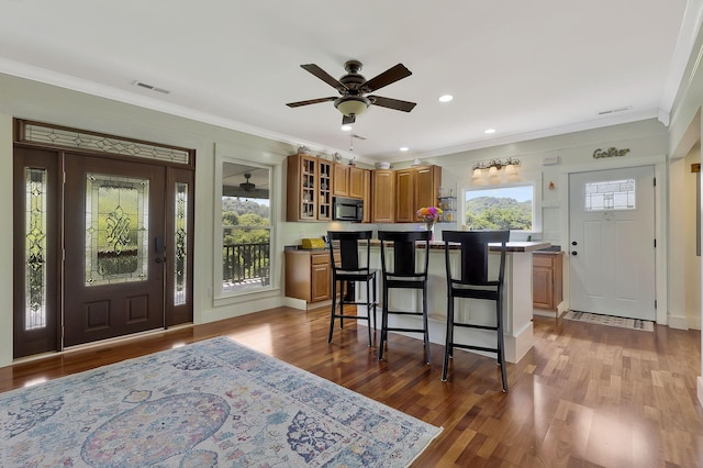 kitchen with a kitchen island, a kitchen bar, ornamental molding, ceiling fan, and light hardwood / wood-style floors