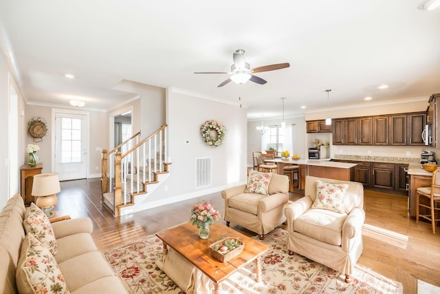 living room with crown molding, ceiling fan with notable chandelier, and light hardwood / wood-style floors