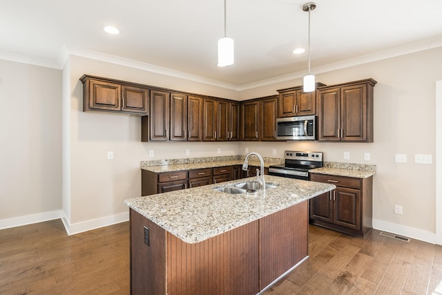 kitchen with sink, appliances with stainless steel finishes, dark hardwood / wood-style floors, light stone countertops, and a kitchen island with sink