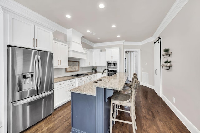 kitchen featuring sink, appliances with stainless steel finishes, white cabinetry, a kitchen island with sink, and a barn door