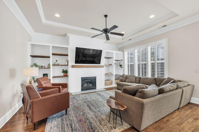 living room with a raised ceiling, ornamental molding, dark wood-type flooring, and a fireplace