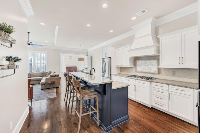 kitchen featuring stainless steel appliances, an island with sink, premium range hood, and white cabinets