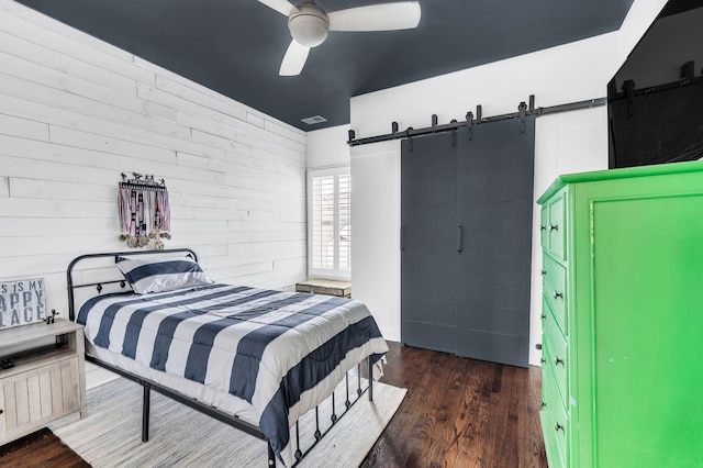 bedroom featuring dark hardwood / wood-style flooring, a barn door, ceiling fan, and wood walls