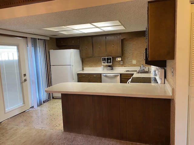 kitchen with dark brown cabinetry, sink, white appliances, and kitchen peninsula