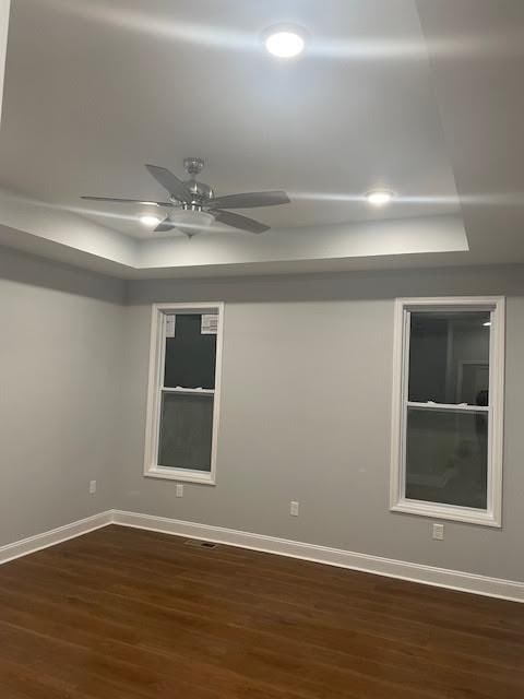 unfurnished room with a ceiling fan, baseboards, and dark wood-type flooring