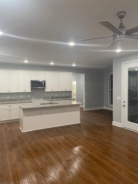 kitchen featuring a center island with sink, white cabinets, ceiling fan, stainless steel microwave, and dark wood-type flooring