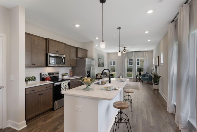 kitchen with sink, a breakfast bar, appliances with stainless steel finishes, a kitchen island with sink, and hanging light fixtures