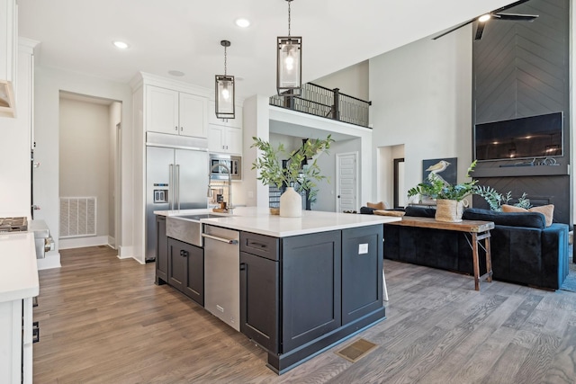 kitchen with white cabinetry, built in appliances, a center island, hanging light fixtures, and light wood-type flooring