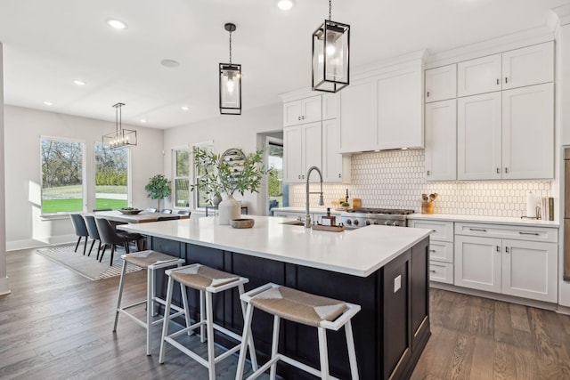 kitchen with dark wood-type flooring, tasteful backsplash, decorative light fixtures, a kitchen island with sink, and white cabinets