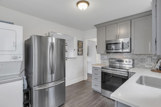 kitchen featuring stacked washing maching and dryer, sink, gray cabinetry, backsplash, and stainless steel appliances