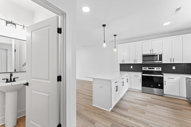 kitchen featuring pendant lighting, white cabinets, decorative backsplash, kitchen peninsula, and stainless steel appliances