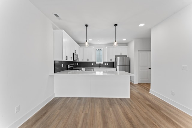 kitchen featuring hanging light fixtures, stainless steel appliances, kitchen peninsula, and white cabinets