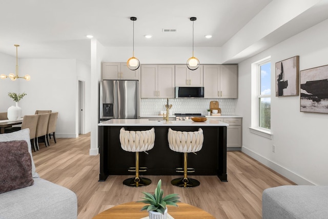 kitchen featuring tasteful backsplash, a center island with sink, stainless steel fridge, gray cabinets, and light hardwood / wood-style floors