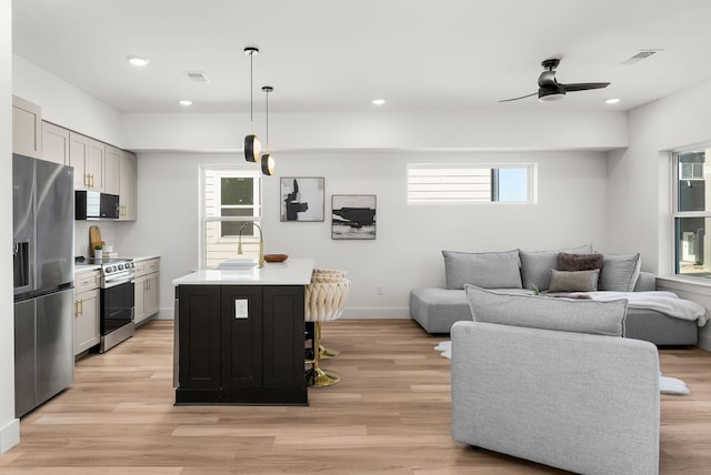 interior space featuring decorative light fixtures, stainless steel appliances, white cabinets, and a center island with sink