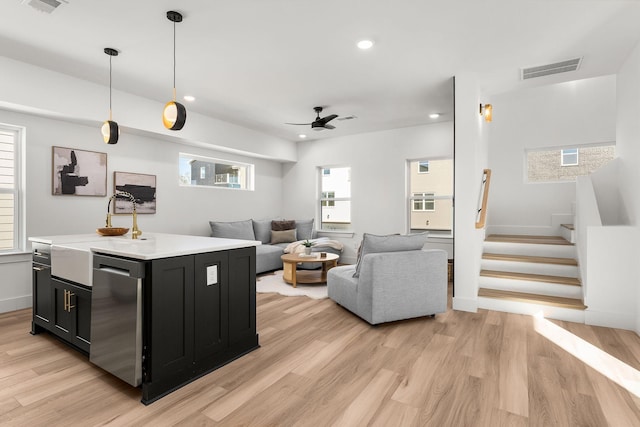 kitchen featuring stainless steel dishwasher, decorative light fixtures, light hardwood / wood-style floors, and a kitchen island with sink