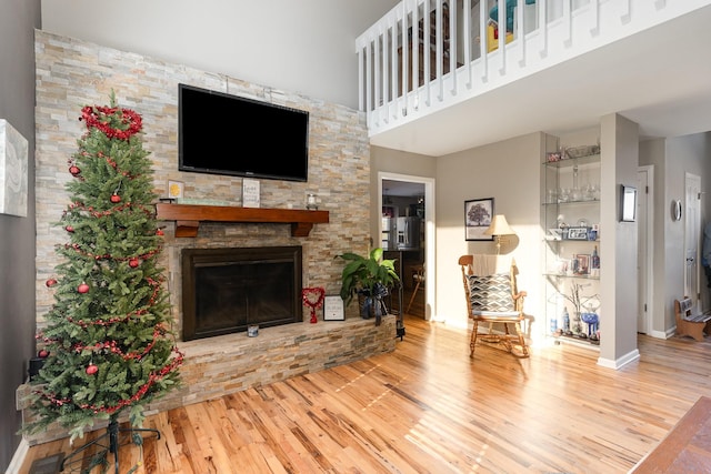 living room featuring a stone fireplace, a towering ceiling, and light wood-type flooring