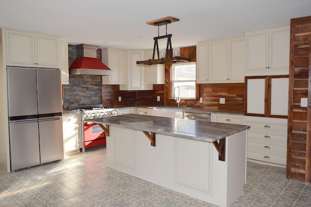 kitchen with wall chimney range hood, hanging light fixtures, a kitchen island, stainless steel appliances, and a kitchen bar