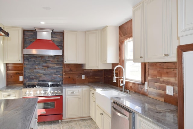 kitchen featuring stainless steel appliances, sink, cream cabinets, and wall chimney range hood