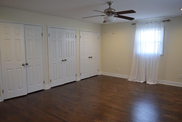 unfurnished bedroom featuring ceiling fan, dark hardwood / wood-style floors, and multiple closets